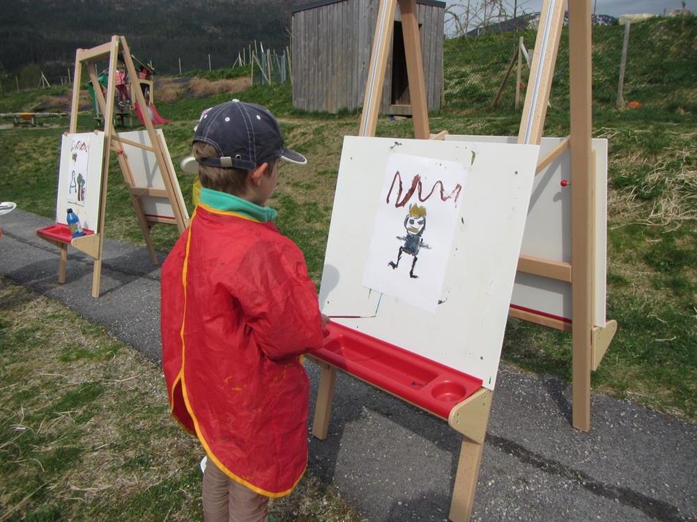 Eit barn står og målar bilde på uteleikeplassen til barnehagen - Klikk for stort bilete